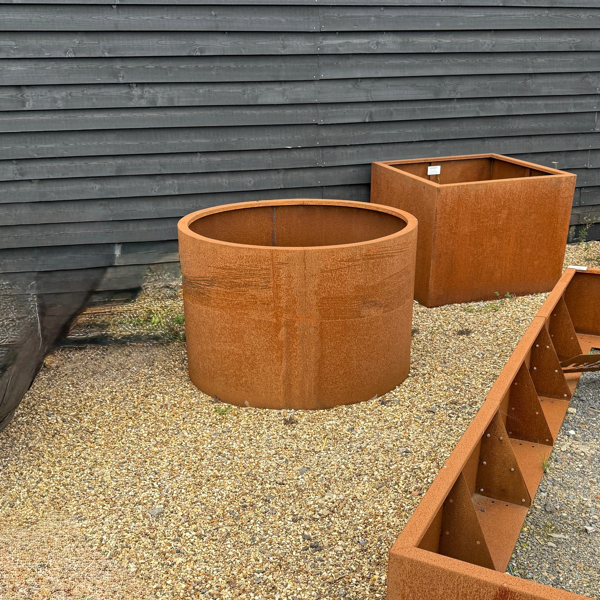 Rust-colored Corten metal planters on a gravel surface against a wooden fence.