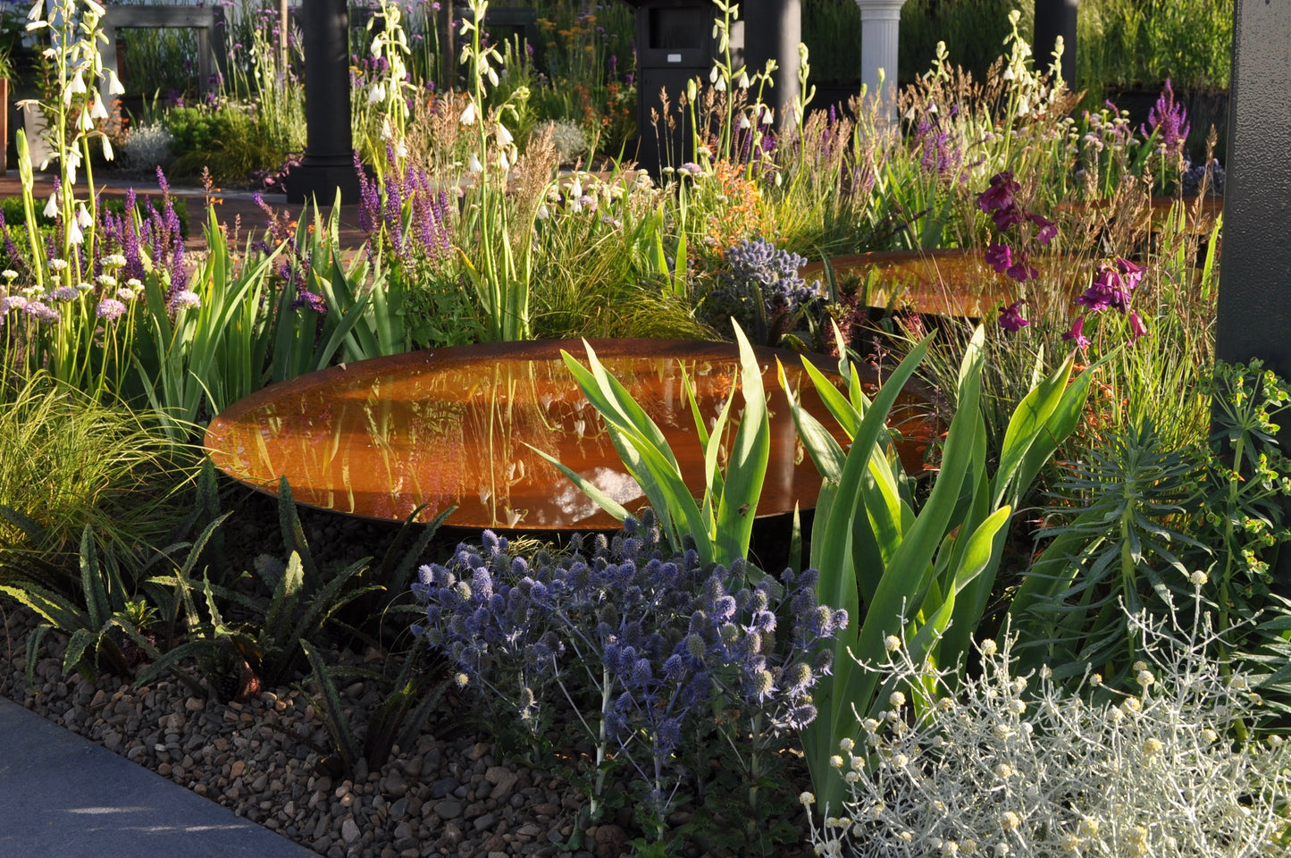 Corten Steel Water Bowl nestled amung spring plants, bathed in sunshine.